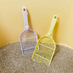 Two pet litter scoops, one white and one yellow, on a bed of cat litter against a yellow background.